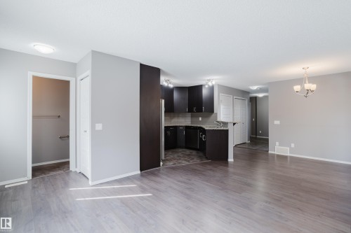 This property features an open living space with light-colored flooring, leading into a kitchen area with dark cabinetry and countertops - 14007 164 Avenue, Edmonton, AB - Indoor