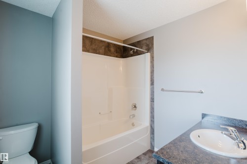 Bathroom featuring a white bathtub with a shower, dark tiled surround, and a vanity with a white sink and chrome faucet - 14007 164 Avenue, Edmonton, AB - Indoor Photo Showing Bathroom