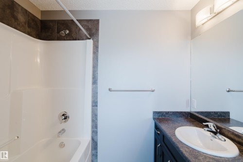 Bathroom with a white shower and tub combination, dark tiled shower surround, and a vanity with a dark countertop and white sink - 14007 164 Avenue, Edmonton, AB - Indoor Photo Showing Bathroom