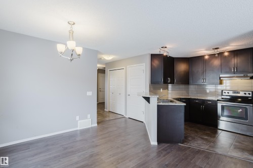 Spacious room with light gray walls and wood-style flooring, featuring a kitchen with dark cabinetry, stainless steel appliances, and a tiled backsplash - 14009 164 Avenue, Edmonton, AB - Indoor Photo Showing Kitchen