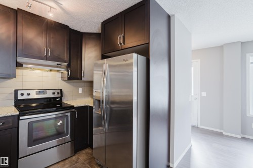The kitchen features dark cabinetry, granite countertops, a tile backsplash, and stainless steel appliances - 14009 164 Avenue, Edmonton, AB - Indoor Photo Showing Kitchen
