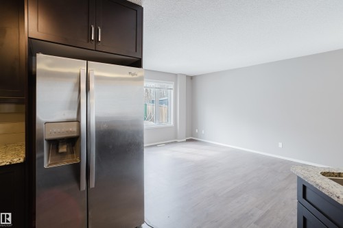 The property features a stainless steel side-by-side refrigerator, dark wood cabinetry, and a granite countertop - 14009 164 Avenue, Edmonton, AB - Indoor