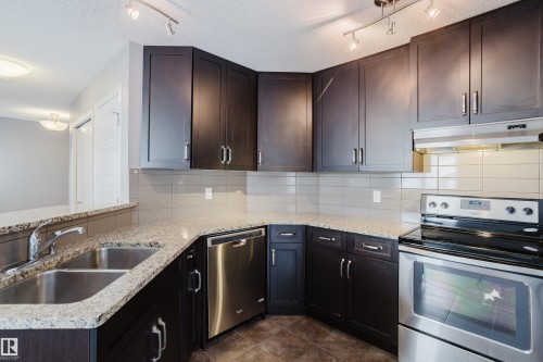 The kitchen features dark wood cabinetry, granite countertops, a double stainless steel sink, a stainless steel dishwasher, and a stainless steel oven with an overhead range hood - 14009 164 Avenue, Edmonton, AB - Indoor Photo Showing Kitchen With Double Sink With Upgraded Kitchen