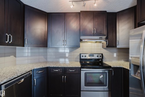 The kitchen features dark cabinetry with silver hardware, granite countertops, and stainless steel appliances including a range, dishwasher, and refrigerator - 14009 164 Avenue, Edmonton, AB - Indoor Photo Showing Kitchen With Upgraded Kitchen