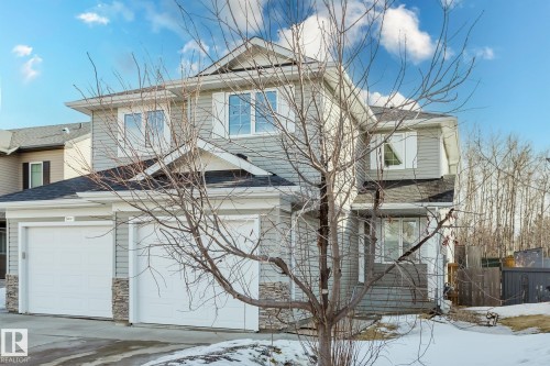 The property features a two-story exterior with light gray siding and stone accents, a dark shingle roof, and white-paneled garage doors - 14009 164 Avenue, Edmonton, AB - Outdoor
