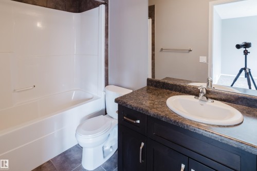 The bathroom features a white bathtub and toilet, a dark vanity with a white oval sink, and a large mirror - 14009 164 Avenue, Edmonton, AB - Indoor Photo Showing Bathroom