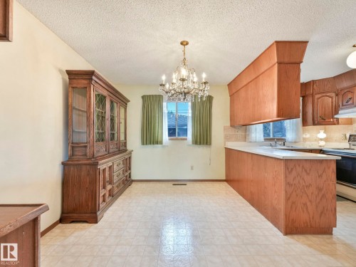 The property features an open-concept living area with a chandelier, a window with curtains, and a kitchen area with wood cabinetry and a counter - 5904 84 Avenue, Edmonton, AB - Indoor Photo Showing Kitchen