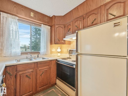The kitchen features wood cabinetry, a double basin sink, and a refrigerator with a top freezer - 5904 84 Avenue, Edmonton, AB - Indoor Photo Showing Kitchen With Double Sink