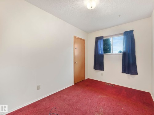 This room features a window with blue curtains, carpeted flooring, and a wooden door - 5904 84 Avenue, Edmonton, AB - Indoor Photo Showing Other Room