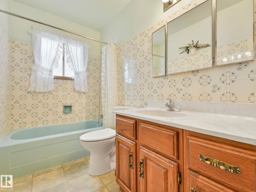 The bathroom features a light blue bathtub, white toilet, and a vanity with a white countertop and wood cabinetry - 5904 84 Avenue, Edmonton, AB - Indoor Photo Showing Bathroom