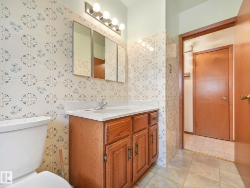 Bathroom featuring patterned tile walls, a vanity with a white countertop and wood cabinetry, and a mirrored medicine cabinet with integrated lighting - 5904 84 Avenue, Edmonton, AB - Indoor Photo Showing Bathroom