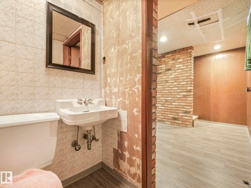 This area features a wall-mounted sink with a mirror above, set against a tiled wall - 5904 84 Avenue, Edmonton, AB - Indoor Photo Showing Bathroom