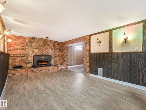 This room features light-colored flooring, a brick and stone fireplace with a black insert, and wood paneling on the walls - 5904 84 Avenue, Edmonton, AB - Indoor Photo Showing Other Room With Fireplace