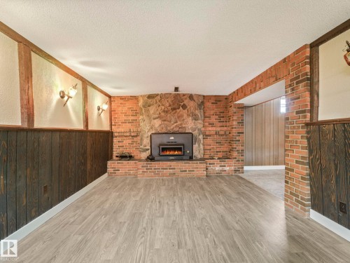 Living area featuring light-colored flooring, exposed brick, and a stone fireplace with a wood-burning insert - 5904 84 Avenue, Edmonton, AB - Indoor With Fireplace
