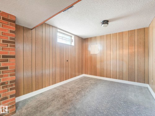 Living area featuring light wood paneling, a gray carpet, and a brick accent wall - 5904 84 Avenue, Edmonton, AB - Indoor Photo Showing Other Room