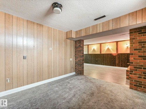 This interior space features light-colored wood paneling, a textured ceiling, and a brick column - 5904 84 Avenue, Edmonton, AB - Indoor Photo Showing Other Room