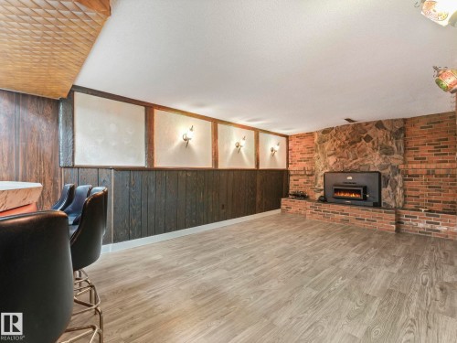 This spacious room features light wood-look flooring, a brick and stone fireplace with an electric insert, and dark wood paneling - 5904 84 Avenue, Edmonton, AB - Indoor With Fireplace