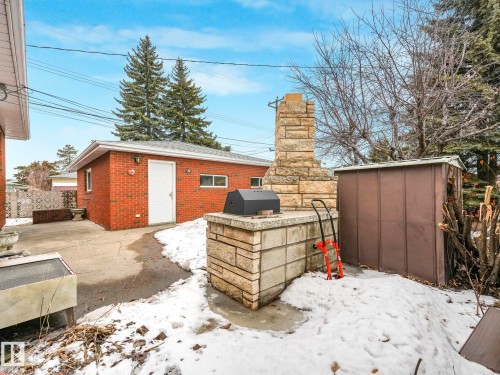 The property features a red brick outbuilding with a white door and white-framed windows, and a built-in stone outdoor cooking area with a chimney - 5904 84 Avenue, Edmonton, AB - Outdoor
