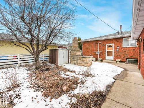 The property features a brick exterior, a paved walkway, and a stone planter with a chimney structure - 5904 84 Avenue, Edmonton, AB - Outdoor