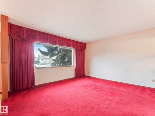 The property features a spacious room with wall-to-wall carpeting, a large window providing ample natural light, and elegant red drapery with a valance - 5904 84 Avenue, Edmonton, AB - Indoor Photo Showing Other Room