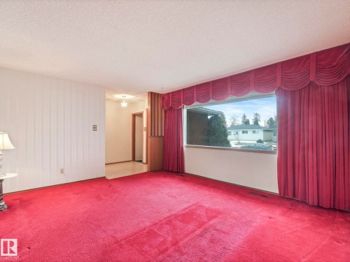 The living area features a large window with drapes, carpeting, and light-colored walls - 5904 84 Avenue, Edmonton, AB - Indoor Photo Showing Other Room