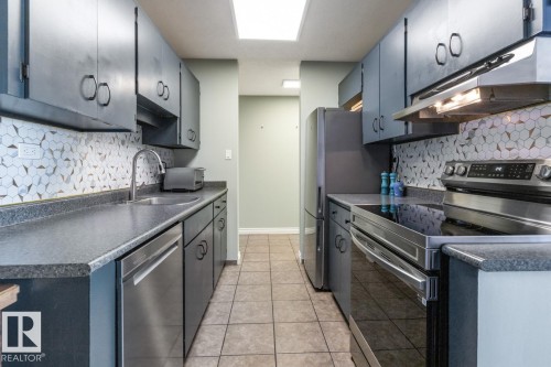 Kitchen featuring stainless steel appliances, dark countertops, tasteful backsplash, and light tile patterned floors - 1207 12303 Jasper Avenue, Edmonton, AB - Indoor Photo Showing Kitchen With Stainless Steel Kitchen