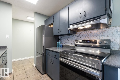Kitchen featuring stainless steel appliances, dark countertops, tasteful backsplash, and light tile patterned flooring - 1207 12303 Jasper Avenue, Edmonton, AB - Indoor Photo Showing Kitchen With Stainless Steel Kitchen