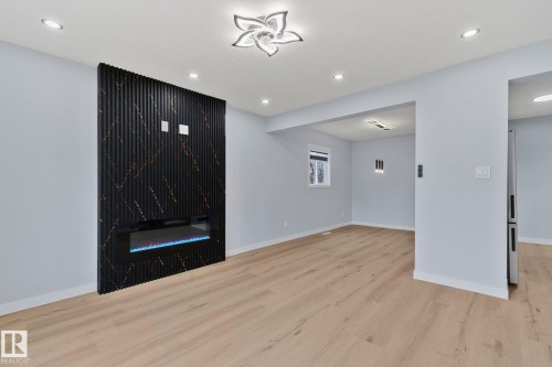 Living area featuring light wood flooring, an electric fireplace with a black accent wall, recessed lighting, and a modern ceiling light fixture - 8620 38A Avenue, Edmonton, AB - Indoor Photo Showing Other Room