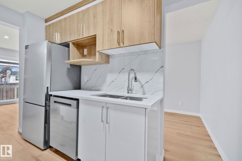 This kitchen features wood-look upper cabinetry, white lower cabinetry, a stainless steel refrigerator, and a stainless steel dishwasher - 8620 38A Avenue, Edmonton, AB - Indoor Photo Showing Kitchen With Double Sink