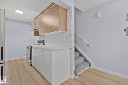 The kitchen features light wood cabinetry, a white countertop, and a white tile backsplash, with light wood flooring extending throughout the space - 8620 38A Avenue, Edmonton, AB - Indoor Photo Showing Kitchen