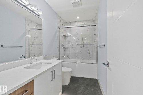 Bathroom featuring a vanity with a white countertop, a mirror with contemporary lighting, and a shower-bathtub combination with a sliding glass door - 8620 38A Avenue, Edmonton, AB - Indoor Photo Showing Bathroom