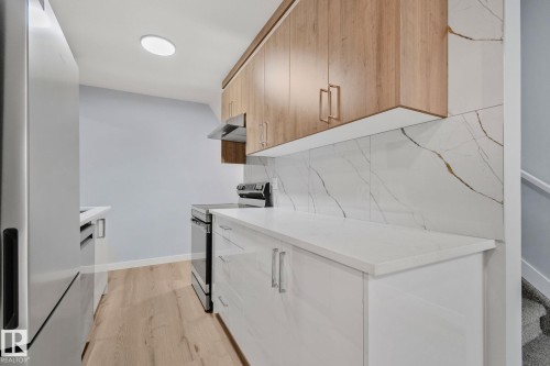 The kitchen features light wood tone upper cabinetry with gold-toned hardware, white lower cabinetry, and white countertops - 8620 38A Avenue, Edmonton, AB - Indoor Photo Showing Kitchen