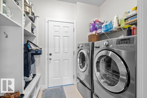 This dedicated laundry area features front-loading washing and drying machines, built-in shelving, and a coat rack for added utility - 1227 Secord Landing, Edmonton, AB - Indoor Photo Showing Laundry Room