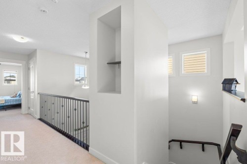 This interior hallway features light-colored carpeting, white walls, and a black wrought iron railing - 1227 Secord Landing, Edmonton, AB - Indoor Photo Showing Other Room