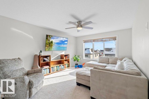 The living room features ample natural light from a large window, a ceiling fan with integrated lighting, and neutral-toned carpet flooring - 1227 Secord Landing, Edmonton, AB - Indoor Photo Showing Living Room