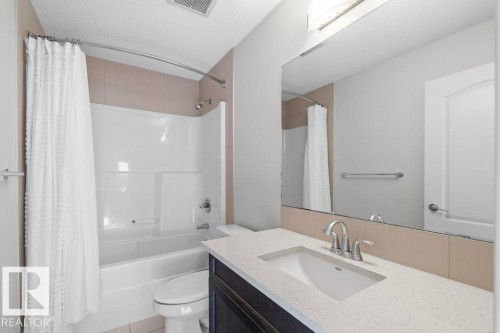 Bathroom featuring a white shower-over-bath, a dark wood vanity with an integrated sink, a light-colored countertop, and a large wall-mounted mirror - 1227 Secord Landing, Edmonton, AB - Indoor Photo Showing Bathroom