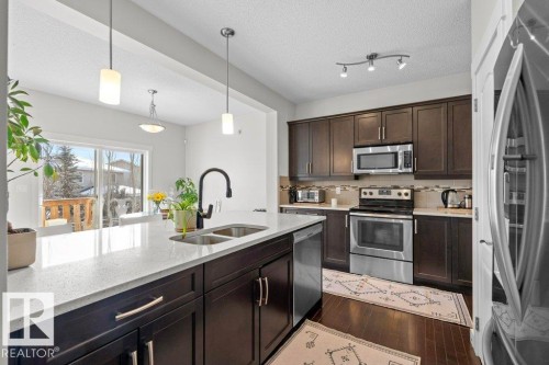 The kitchen features dark wood cabinetry, stainless steel appliances, and a light-colored countertop - 1227 Secord Landing, Edmonton, AB - Indoor Photo Showing Kitchen With Double Sink With Upgraded Kitchen