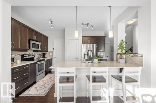 The kitchen features dark wood cabinetry, stainless steel appliances, and a light-colored island with seating - 1227 Secord Landing, Edmonton, AB - Indoor Photo Showing Kitchen With Upgraded Kitchen