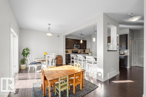The dining area features dark hardwood flooring and a large window providing natural light, with a view into the kitchen area - 1227 Secord Landing, Edmonton, AB - Indoor Photo Showing Dining Room