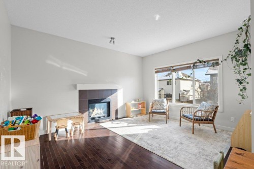 Living area featuring rich hardwood floors, a contemporary fireplace with a dark tile surround, and a large window providing natural light - 1227 Secord Landing, Edmonton, AB - Indoor Photo Showing Living Room With Fireplace