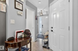 The entryway features a white panel door with black hardware, light-colored flooring, and a decorative overhead light fixture - 