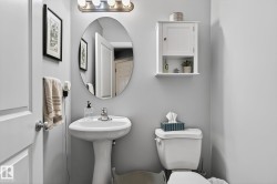 Well-maintained bathroom featuring a pedestal sink, an oval mirror, and a wall-mounted cabinet with open shelving - 