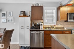 The kitchen features wood cabinetry, a stainless steel dishwasher, and a window with blinds positioned above the sink - 