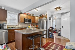 The kitchen features wood cabinetry, stainless steel appliances, and a central island with a countertop - 