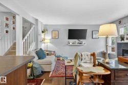 The living area features light-colored walls, hardwood flooring, and a staircase with white railings - 