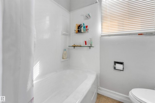 Bathroom featuring a white bathtub, a shower curtain, and a window with horizontal blinds - 12908 126 Street, Edmonton, AB - Indoor Photo Showing Bathroom