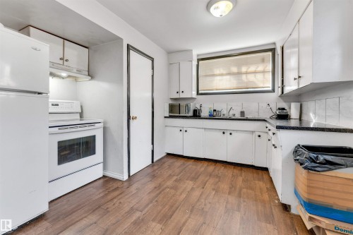 The kitchen features wood-look flooring, white cabinetry with black hardware, a window with blinds, and white appliances including a refrigerator and range - 12908 126 Street, Edmonton, AB - Indoor Photo Showing Kitchen