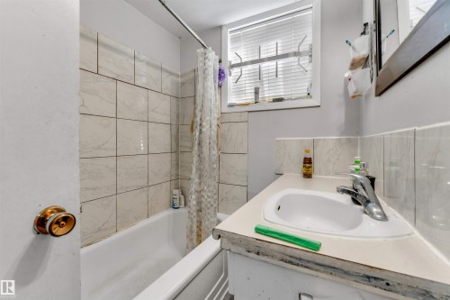 The bathroom features a tiled shower surround, a white bathtub, and a vanity with an integrated sink and chrome faucet - 12908 126 Street, Edmonton, AB - Indoor Photo Showing Bathroom