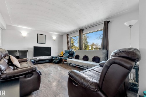 The living room features hardwood flooring, sconce lighting, and large windows that provide views of the outdoors - 12908 126 Street, Edmonton, AB - Indoor Photo Showing Living Room