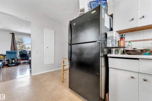 The kitchen features white cabinetry and a black refrigerator, with an adjoining living area visible - 12908 126 Street, Edmonton, AB - Indoor Photo Showing Kitchen
